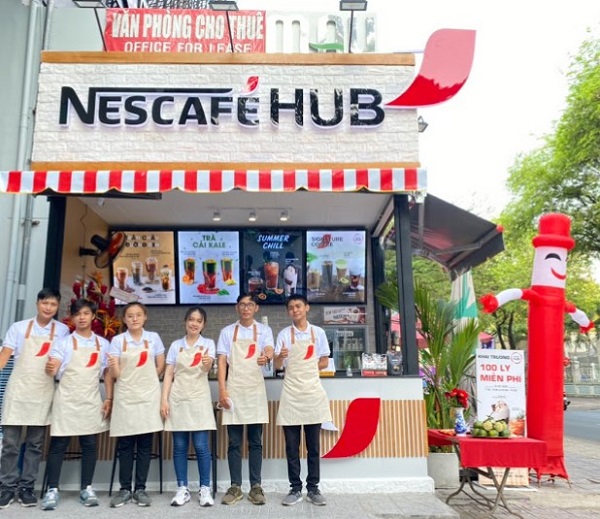 Mẫu đồng phục của nhân viên quán cafe Nescafe HUB thiết kế đơn giản với áo phông trắng, cổ trụ, tạp dề màu kem có vài chi tiết in ấn nổi bật